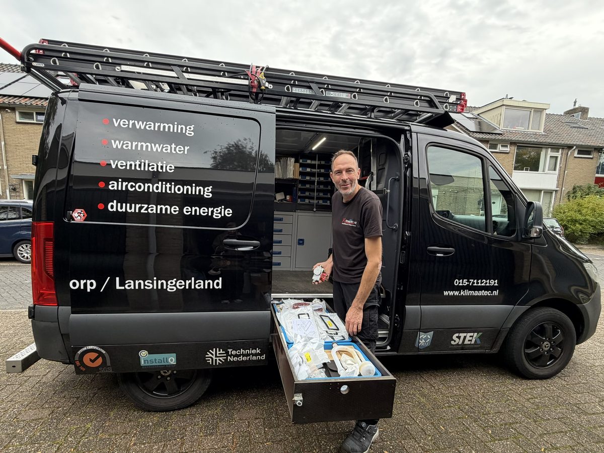 Peter Bloemberg bij de open zijdeur van de KlimaaTec-bus, met een uitgeschoven lade vol netjes gesorteerde onderdelen