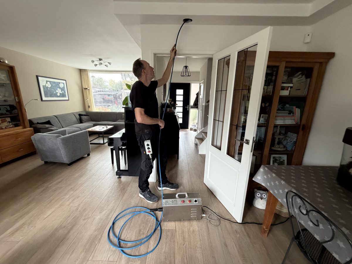 Peter Bloemberg voert de roterende borstel via een plafondventiel het ventilatiekanaal in, met de reinigingsmachine op de vloer